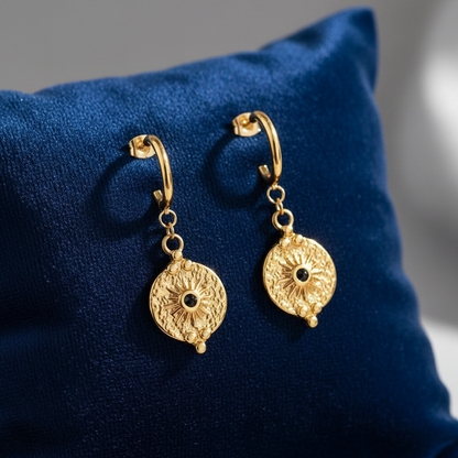 Gold medallion earrings on velvet cushion